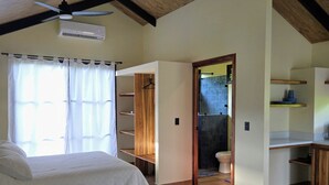 Een slaapkamer met een bed, een plafondventilator, een raam met gordijnen en een houten vloer.