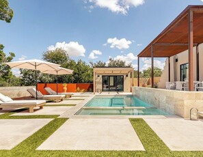 Ein moderner Poolbereich im Freien mit Liegestühlen, einer überdachten Sitzgelegenheit und freiem Blick auf den Pool.