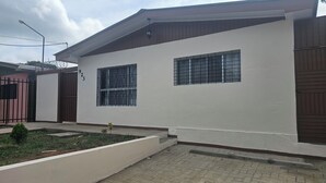 A two-story building with a white exterior, a gated entrance, and a small garden area. - Cozy 3-bedroom house with AC in charming, centrally located Masatepe, (Masatepe)