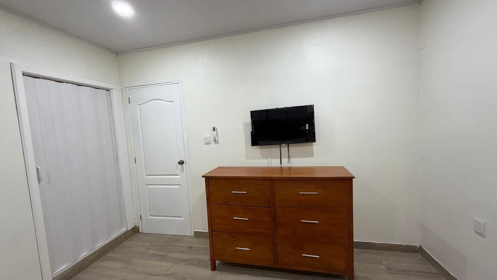 Een kamer met een houten dressoir, een witte deur en een wandtelevisie.