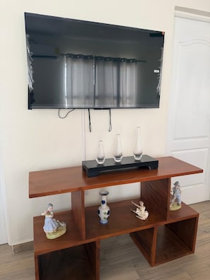 A flat-screen TV mounted on a wall above a wooden TV stand with decorative items.