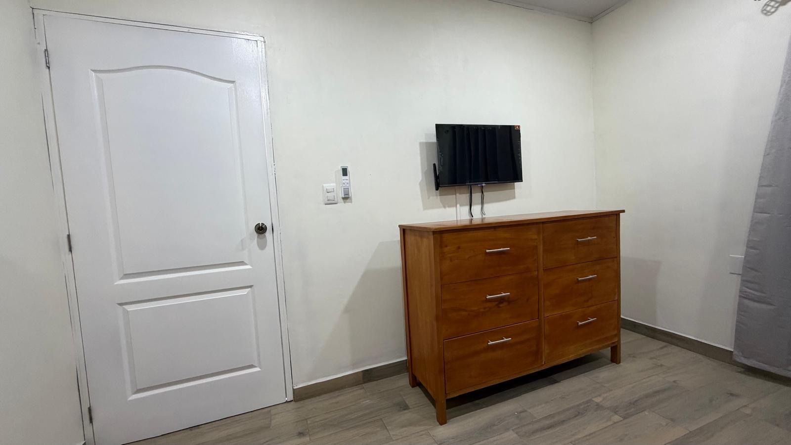 Una stanza con una porta bianca, un comò in legno e una TV a schermo piatto montata a parete.