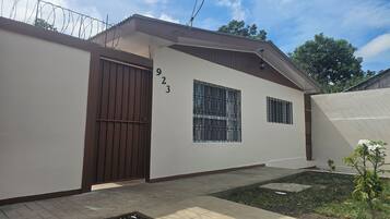 Edificio residencial con una verja marrón, el número '923' en la pared y un pequeño jardín con una planta.