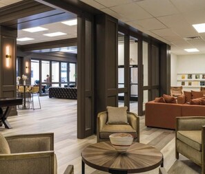 Eine großzügige Lobby mit Sitzgelegenheiten, einem Esstisch und einem großen Fenster für natürliches Licht.