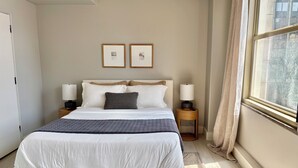 Un dormitorio ordenado con cama, lámparas de noche, alfombra y ventana con cortinas.