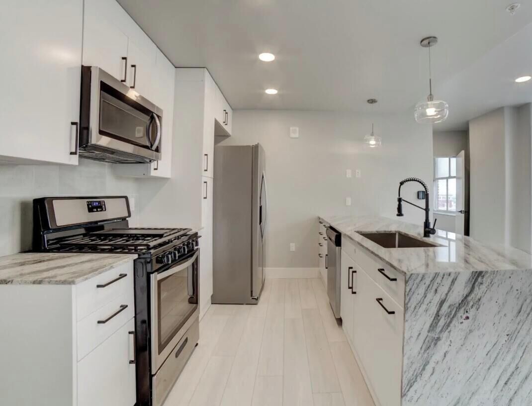 A modern kitchen with white cabinetry, a stainless steel range, a built-in oven, a refrigerator, and a marble countertop.