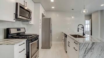 A modern kitchen with white cabinetry, a stainless steel range, a built-in oven, a refrigerator, and a marble countertop.