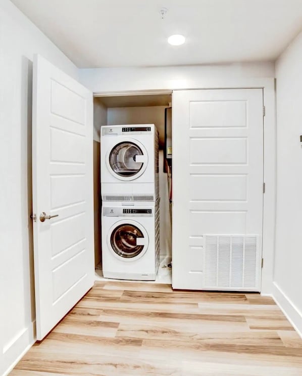 A laundry room with two stacked washing machines and a dryer, wooden flooring, and white walls.