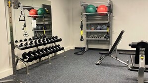 Un gimnasio con equipamiento de levantamiento de pesas, mancuernas y pelotas de ejercicio.