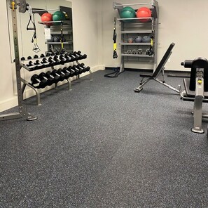 Ein Fitnessraum mit Krafttrainingsgeräten, Hanteln und Übungsbällen.