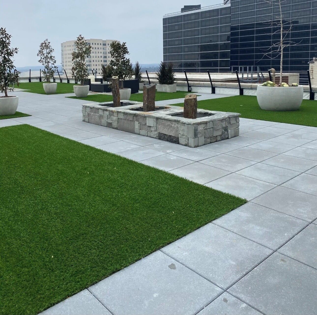 A landscaped outdoor area with artificial grass, stone planters, and a modern building in the background.