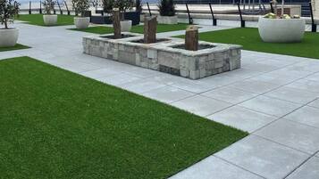 A landscaped outdoor area with artificial grass, stone planters, and a modern building in the background.