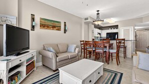 Una sala de estar con televisor, sofá, mesa de centro y comedor con sillas y una mesa.
