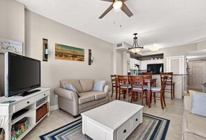Ein Wohnzimmer mit Fernseher, einer Couch, einem Couchtisch und einem Essbereich mit Stühlen und einem Tisch.