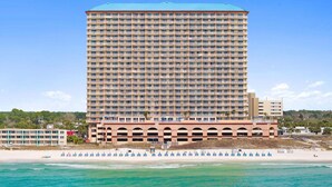 Un hotel moderno con varios balcones, ubicación frente al mar y vista despejada del océano.