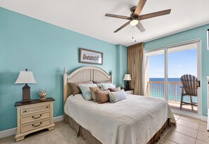 A bedroom with a bed, a nightstand, a lamp, a ceiling fan, a framed picture, and a view of the ocean through a sliding door. - 22nd Floor Gulf-Front Escape, Sunrise Beach Resort, Resort Pools, Sleeps 7 (Panama City Beach)