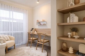 Ein modernes Wohnzimmer mit einer Couch, einem runden Couchtisch, einem Schreibtisch mit zwei Stühlen und einem Bücherregal mit Büchern und Dekoration.