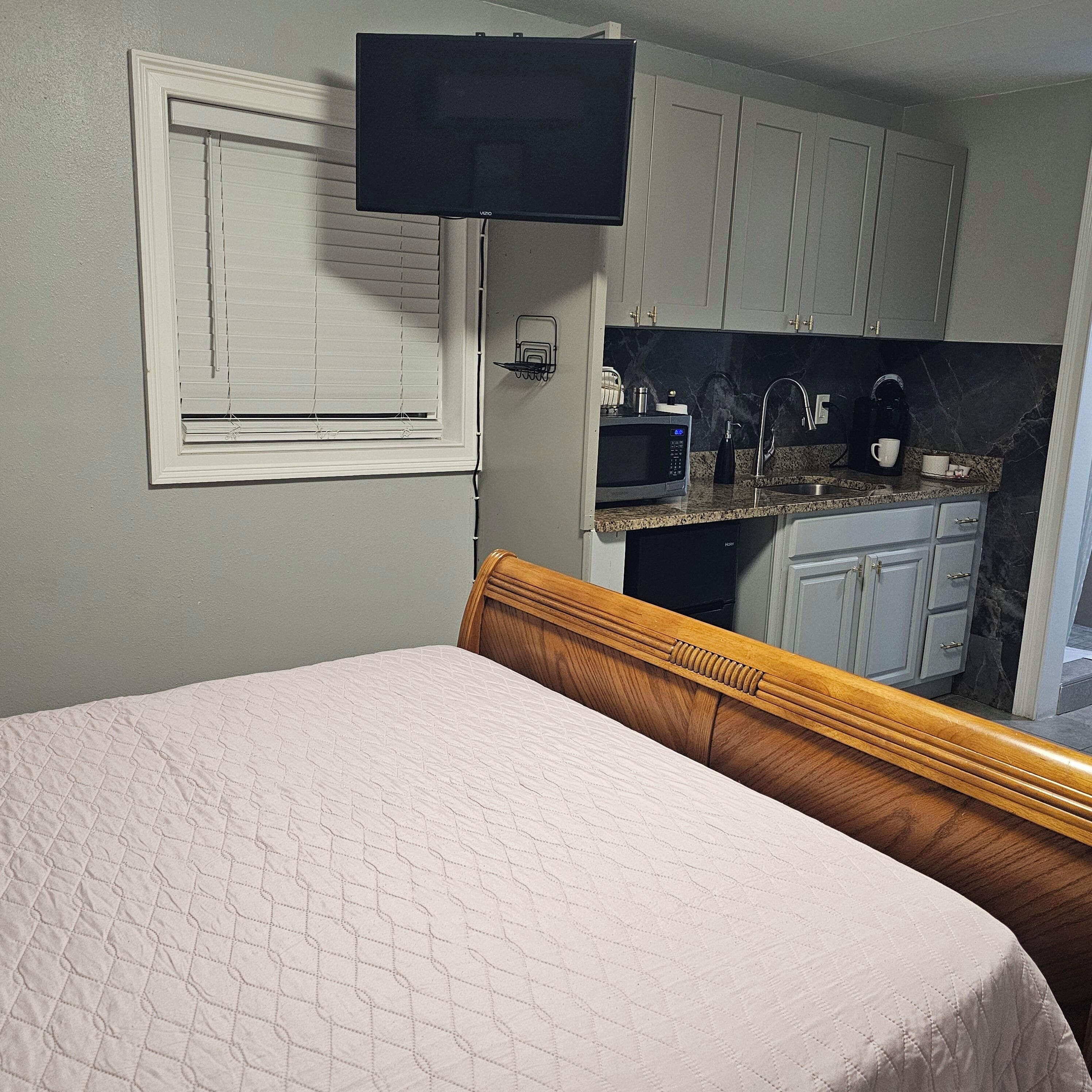 Una camera da letto con un letto, una televisione a muro e un angolo cottura dotato di forno a microonde, lavello e pensili.
