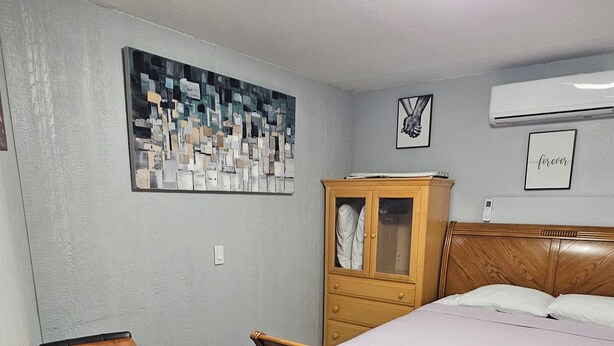 Um quarto com uma cama de madeira, uma mesinha, um armário e um quadro na parede.