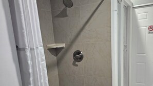 Área de chuveiro com chuveiro manual, prateleira no canto e porta com aviso 'Não Fumar'.