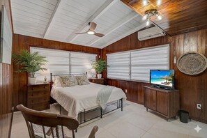 Un dormitorio con cama, televisor, ventilador de techo y ventana con persianas.