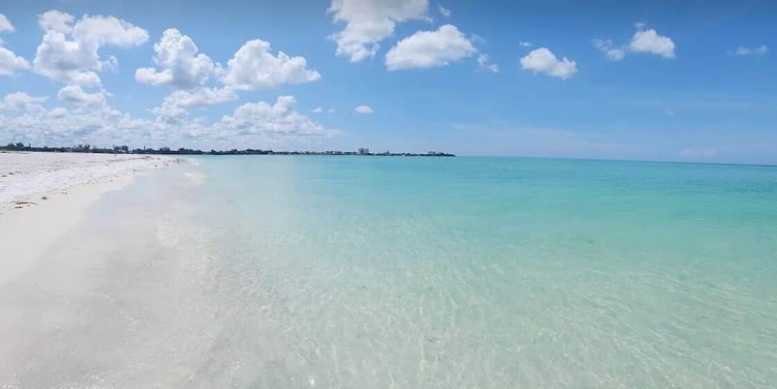 Une plage à l’eau turquoise et limpide, bordée d’un rivage de sable blanc.