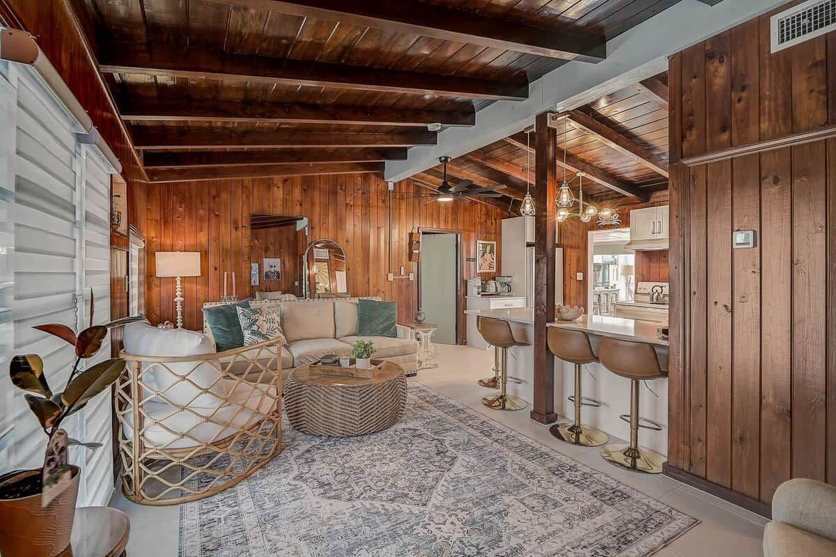 A spacious living area with a wooden ceiling, a sofa set, a coffee table, and a bar area with stools.