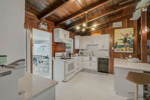 A kitchen with white cabinets, a microwave, a stove, and a dining area with chairs. - Cozy 3BR Sarasota Bungalow near Lido & Siesta (Sarasota)