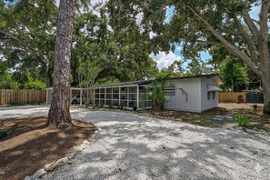 A single-story building with a garage, surrounded by trees and a gravel driveway. - Cozy 3BR Sarasota Bungalow near Lido & Siesta (Sarasota)