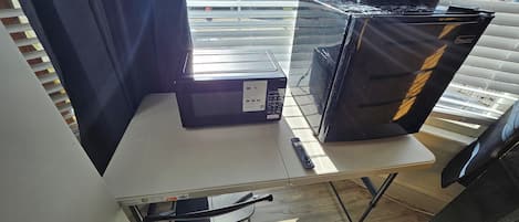 Una habitación con una mesa, un microondas y un refrigerador.