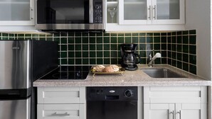 Uma cozinha com armários brancos, micro-ondas de aço inoxidável, cafeteira e lava-louças.