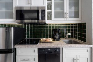 Una cucina con mobili bianchi, un forno a microonde in acciaio inossidabile, una macchina da caffè e una lavastoviglie.