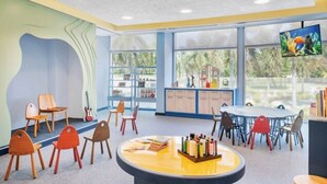 Uma sala de brinquedos infantil com uma mesa redonda, cadeiras e uma televisão.