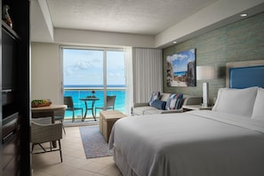 Una camera d'albergo con un letto grande, un balcone vista oceano, un'area pranzo con tavolo e sedie e una televisione.