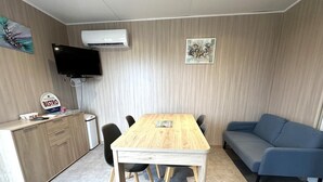 A room with a wooden dining table, chairs, a blue sofa, a TV, and a wall-mounted air conditioner. - The Ribouillet Cabin (CREON D'ARMAGNAC)
