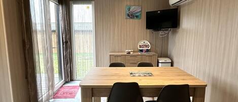 A dining area with a wooden table and four chairs, a television mounted on the wall, and a sign indicating a bistro.