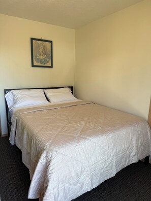 A single bed with a beige quilt, a framed picture on the wall, and a carpeted floor. - Panoramic Ocean Views + Hot Tub: Steps to Beach (Lincoln City)