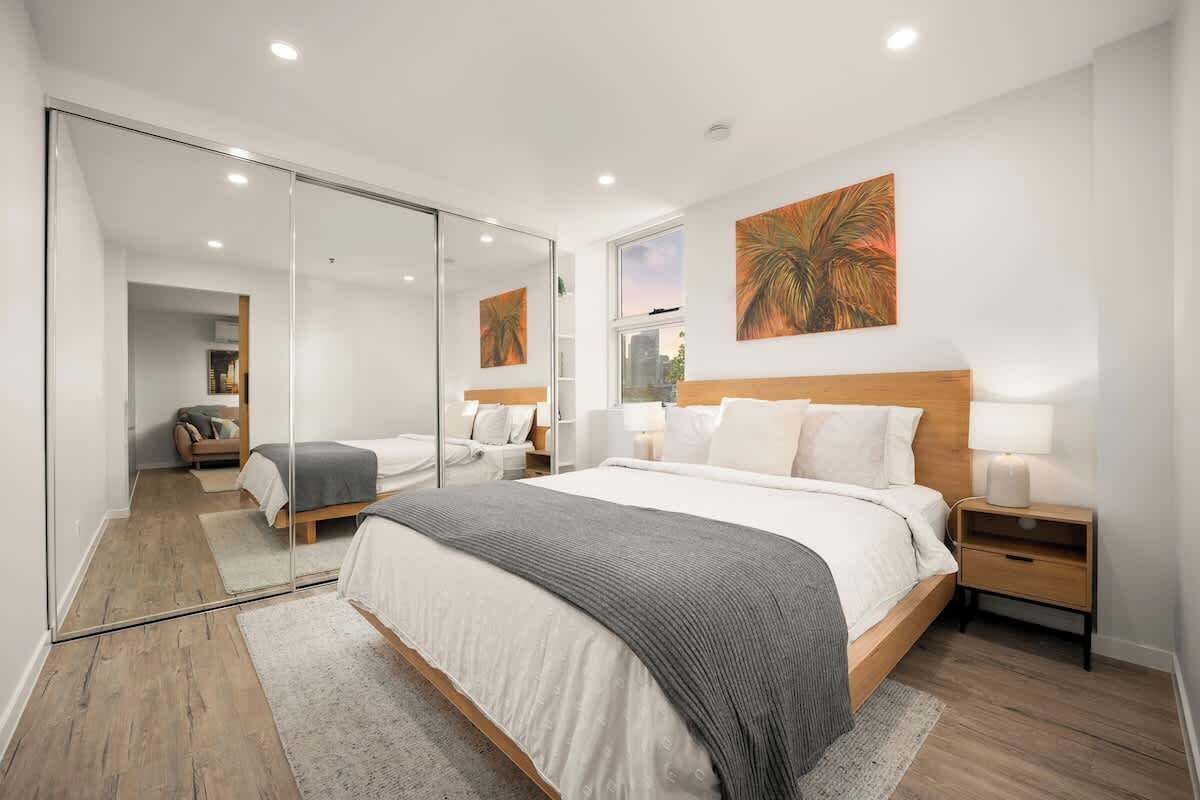 A modern bedroom with a large bed, a mirror, and a city view.