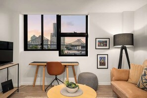 Ein modernes Wohnzimmer mit großem Fenster, einem Schreibtisch, einem Fernseher, einem Sofa und einer Lampe.
