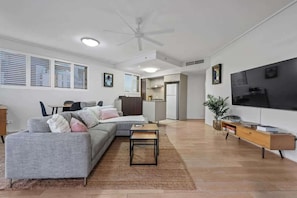 Ein modernes Wohnzimmer mit Sofa, Couchtisch, Fernseher und einer Küche im Hintergrund.