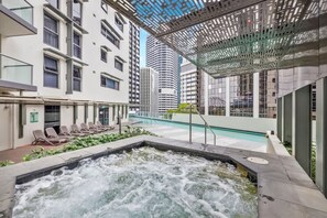 Ein Poolbereich auf dem Dach mit Whirlpool, Liegestühlen und Blick auf die umliegenden Gebäude.