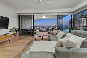 Ein modernes Wohnzimmer mit einer Couch, einem Couchtisch und einem Fernseher. Ein Balkon bietet Blick auf die Stadt.