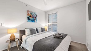 A bedroom with a bed, a nightstand, a lamp, a ceiling fan, a window with blinds, and a painting on the wall. - Breathtaking! 2bed/2bath/1car/balcony/views ~ CBD (Brisbane)