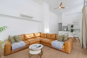 Ein modernes Wohnzimmer mit einem ledernen Ecksofa, einem kleinen runden Couchtisch und einem Deckenventilator.