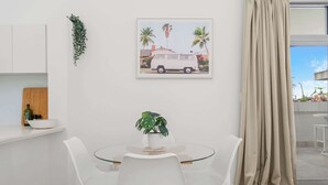 A dining area with a glass table, white chairs, a potted plant, and a framed picture on the wall. - Hidden Oasis 2bed-2bath-1car - 5 Mins to CBD (Brisbane)