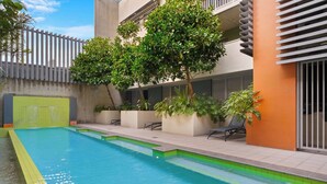 A swimming pool with a tiled edge, surrounded by potted plants and lounge chairs. - Hidden Oasis 2bed-2bath-1car - 5 Mins to CBD (Brisbane)