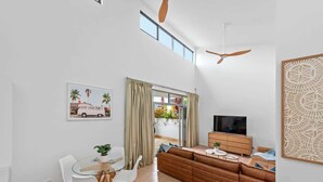 A modern living room with a glass dining table, white chairs, a brown sofa, a TV, and a ceiling fan. - Hidden Oasis 2bed-2bath-1car - 5 Mins to CBD (Brisbane)