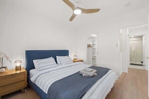 Ein Schlafzimmer mit Bett, Nachttischen, Deckenventilator, einem Nachttisch mit Lampe und einem begehbaren Kleiderschrank.