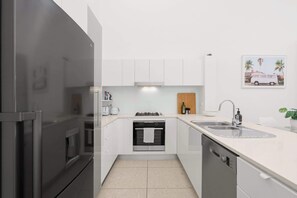 Eine moderne Küche mit weißen Schränken, einem Edelstahlkühlschrank, einem eingebauten Backofen und einem Geschirrspüler.