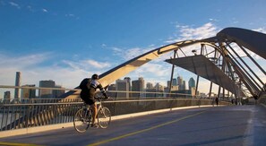 Uma pessoa anda de bicicleta sobre uma ponte, com o horizonte da cidade ao fundo.